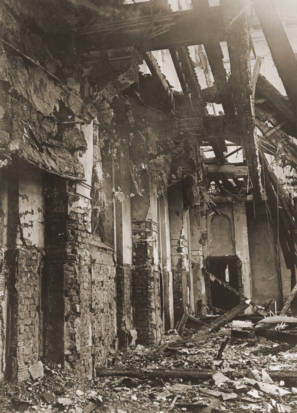 The gutted interior of the same synagogue, roof burned away, galleries and columns standing over a floor of ash and fallen masonry.