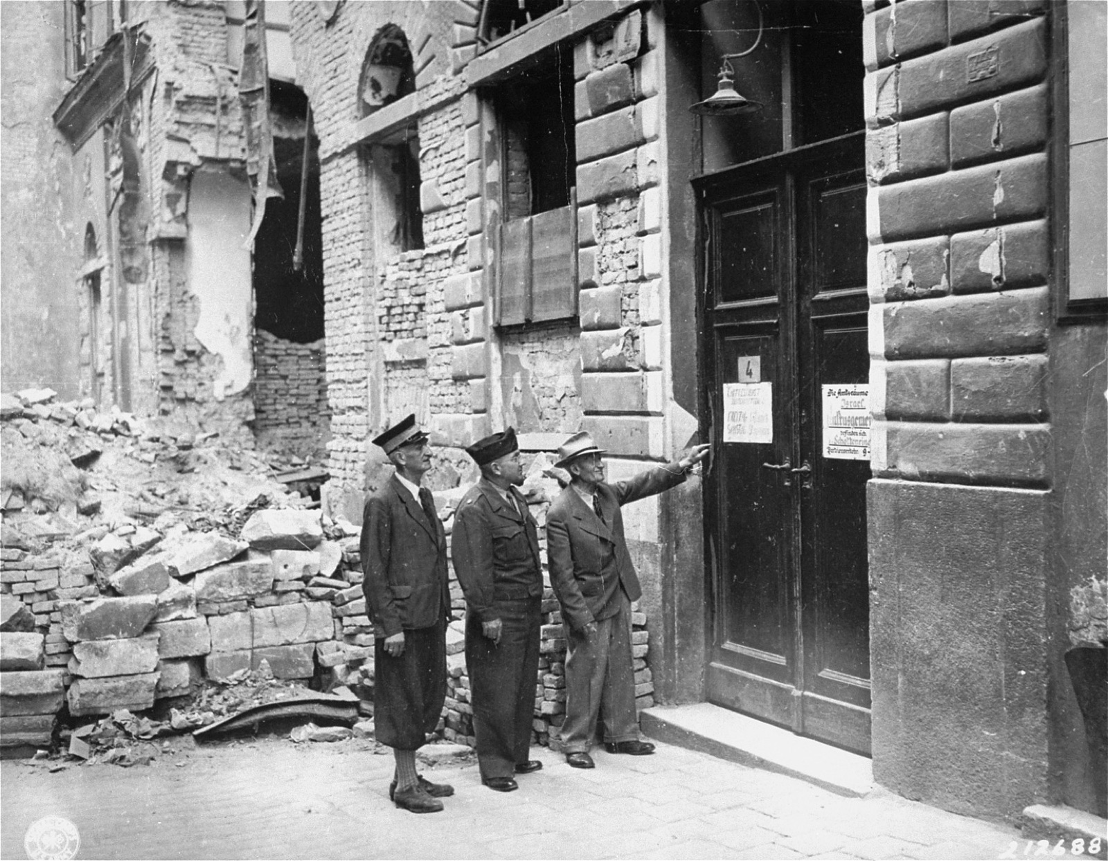 A plain stone building front flush with its neighbors on a narrow city street, a doorway at pavement level with a small sign beside it, no dome, tower or religious ornament on the facade.