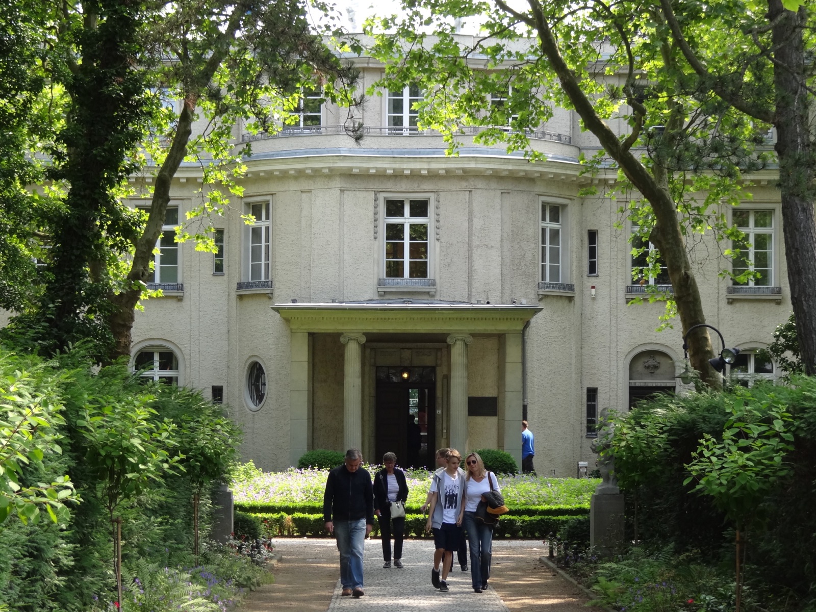 A large white stuccoed villa with a columned portico and a steep hipped roof, seen across a lawn in bright summer light.