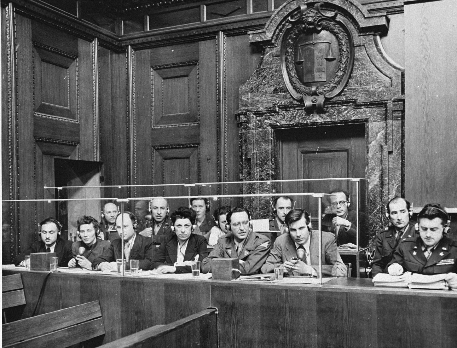 Interpreters seated in a low glass-fronted booth at the side of a courtroom, wearing headsets and speaking into microphones.