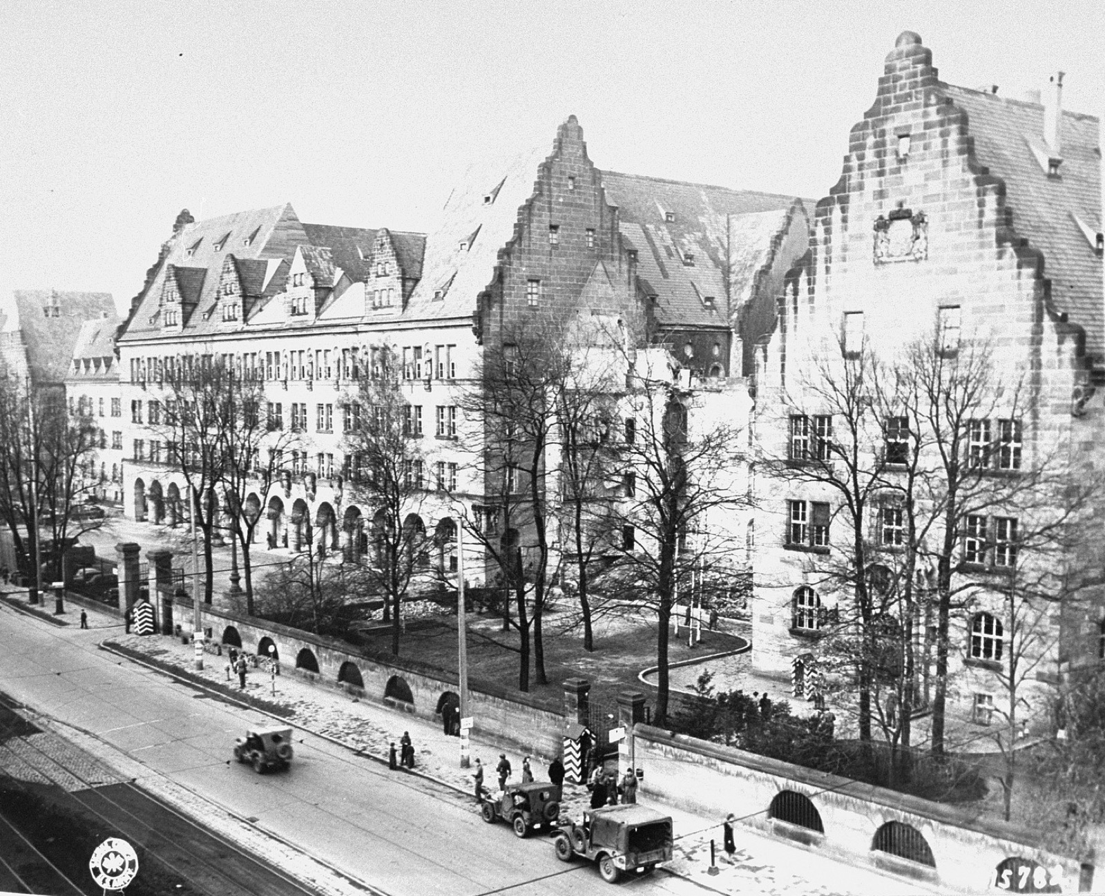 The long stone facade of the Palace of Justice in Nuremberg seen from the street, with military vehicles parked outside.